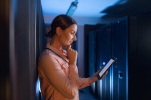 Thoughtful caucasian female engineer using digital tablet in computer server room